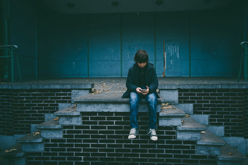 Young boy sitting on abandoned steps looking at cell phone